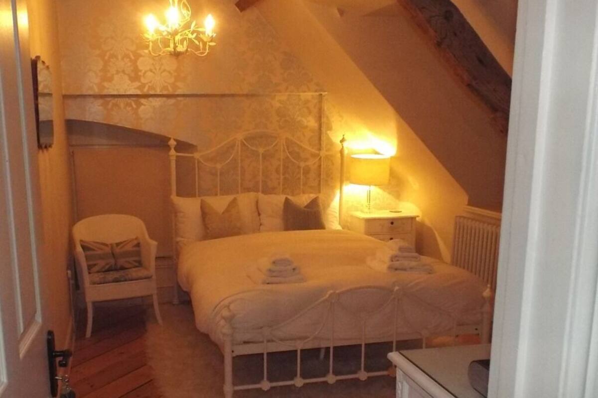 A cozy bedroom with a large bed, a chair, a nightstand, and a chandelier.