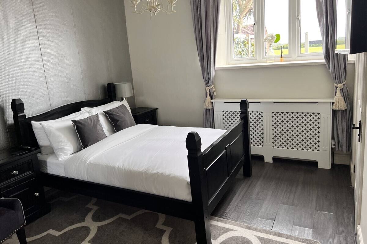 A neatly arranged bedroom with a bed, bedside tables, a lamp, and a window with curtains.