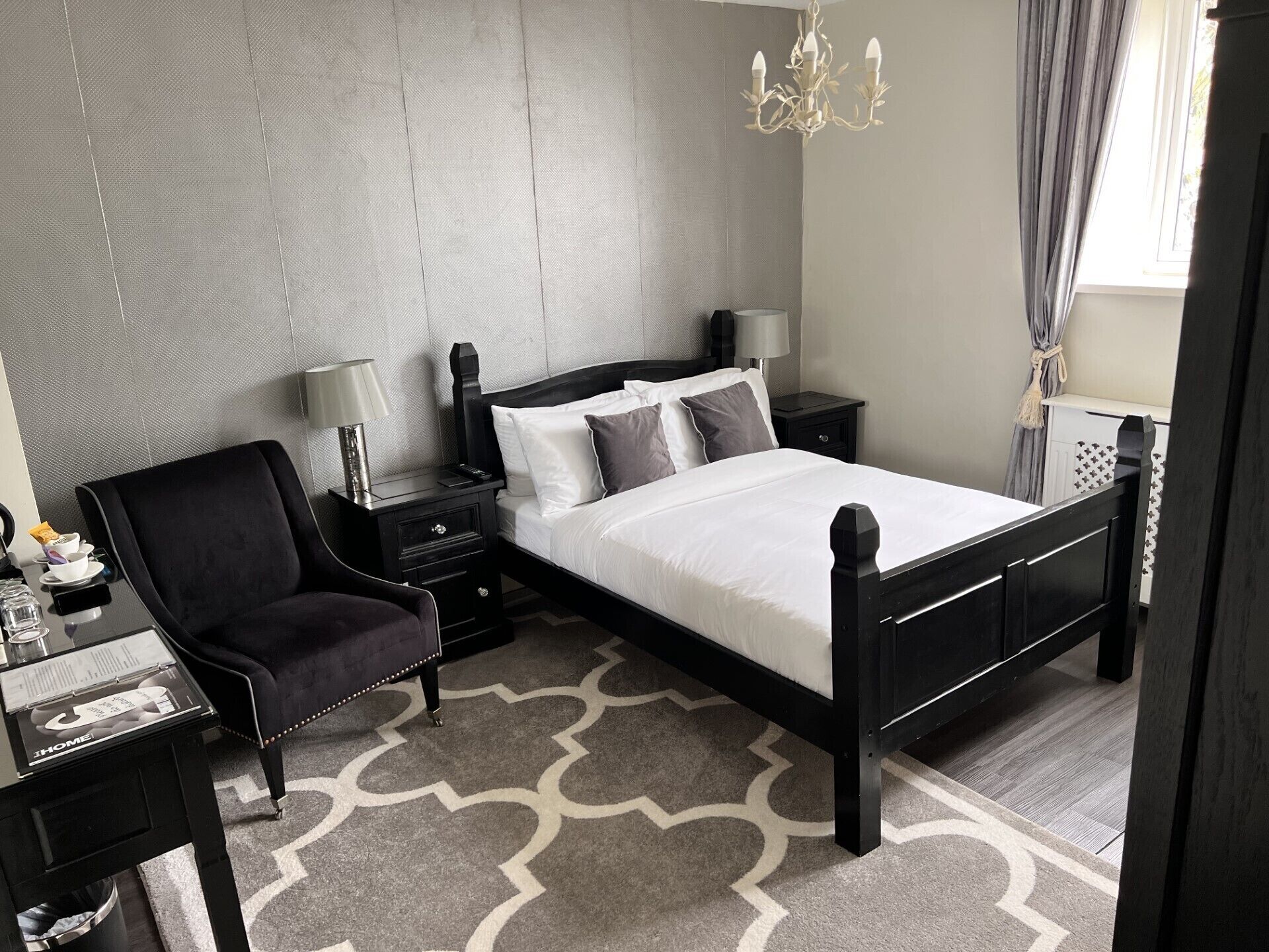 Een keurig opgemaakt slaapkamer met een bed, nachtkastjes, een stoel en een kroonluchter.