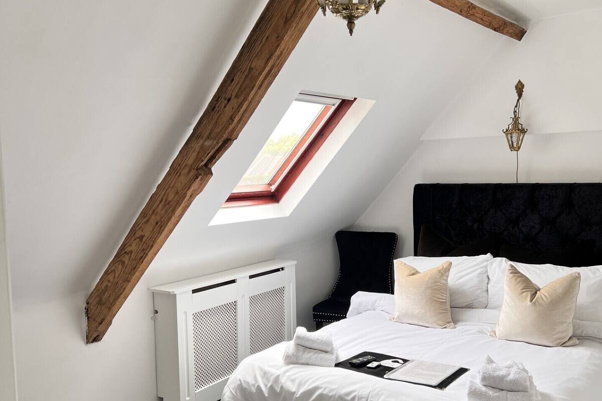 A bedroom with a sloped ceiling, a skylight, a bed with white linens, and a black headboard.