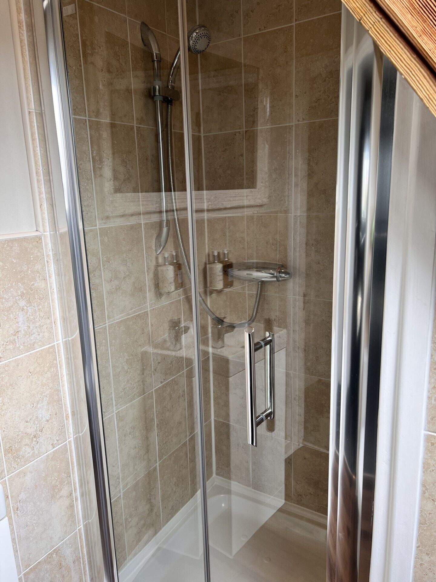A glass-enclosed shower with a handheld showerhead and a wall-mounted faucet.