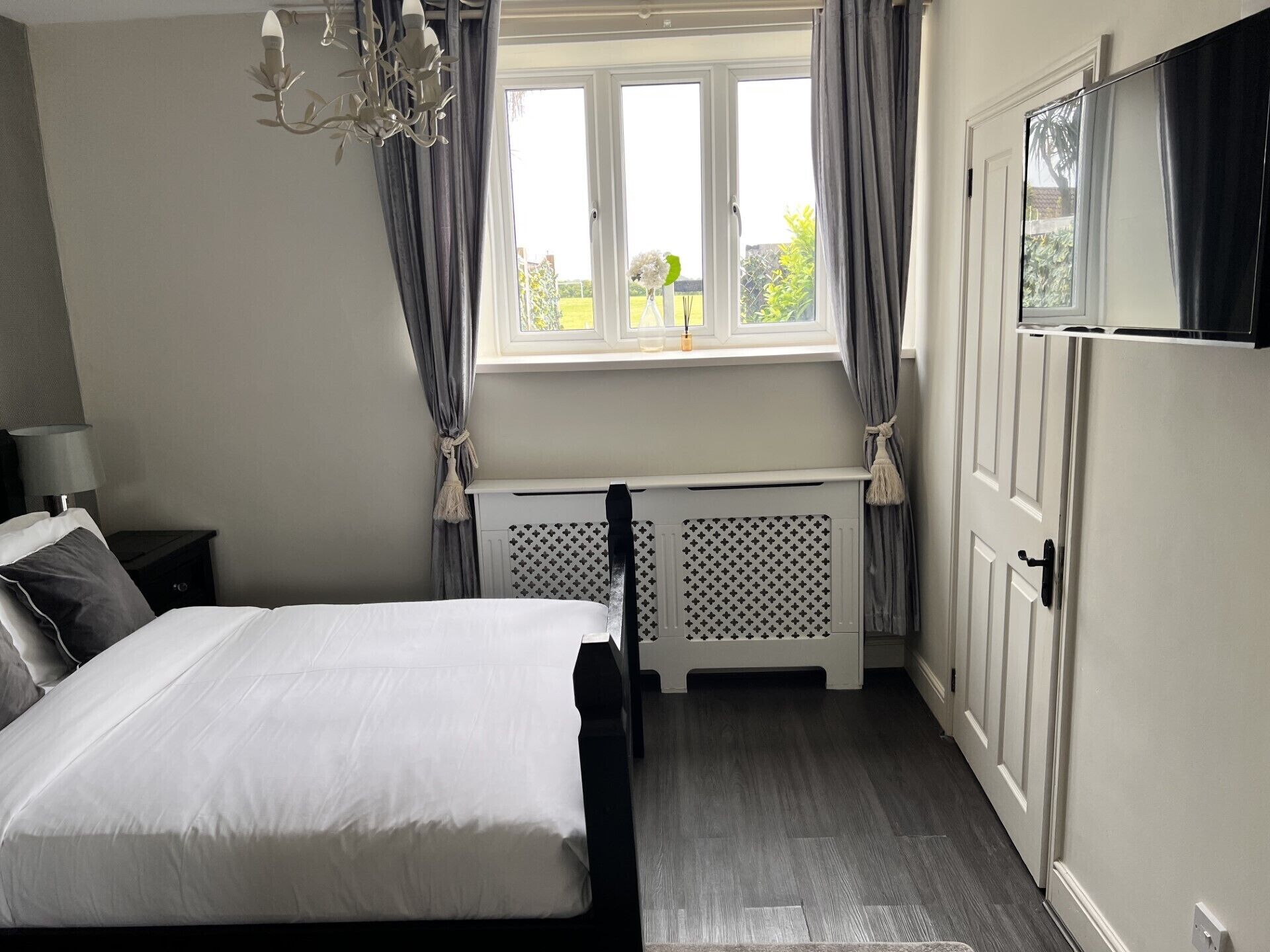 A bedroom with a bed, a nightstand, a dresser, a radiator, and a window with curtains.