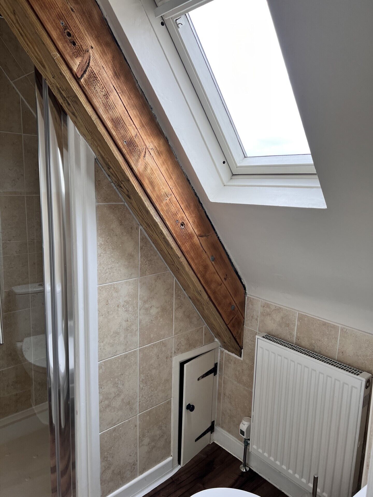 A bathroom with a skylight, wooden beams, a shower, a toilet, and a radiator.