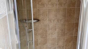 Una ducha con cerramiento de vidrio, azulejos color beige, un cabezal de ducha cromado y una bañera blanca.