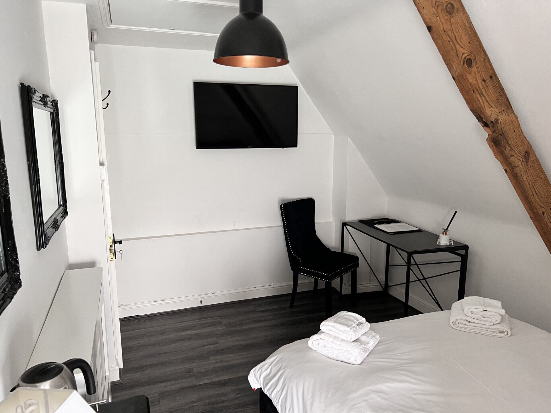 Een moderne slaapkamer met een bed, bureau, stoel, televisie en waterkoker.