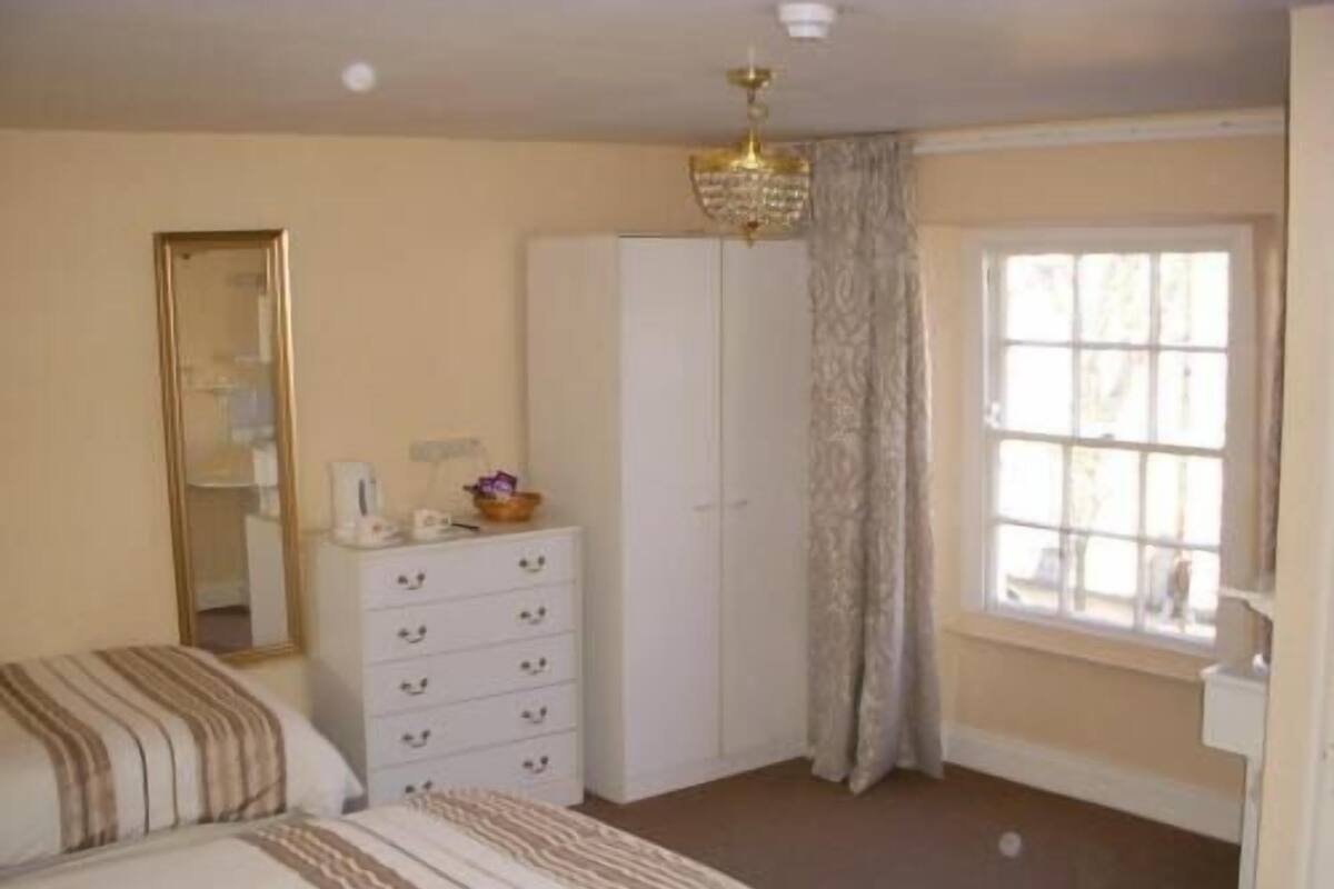 A bedroom with a bed, a dresser, a wardrobe, a window with curtains, and a chandelier.