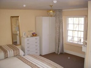 A bedroom with a bed, a dresser, a wardrobe, a window with curtains, and a chandelier.