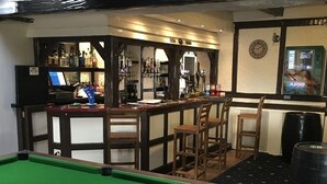 A billiards table, bar area with stools, and a pool table in a room with wooden beams and a clock on the wall. - The Buck INN (Richmond)
