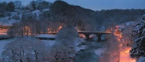 A snow-covered landscape with a bridge and buildings in the background.