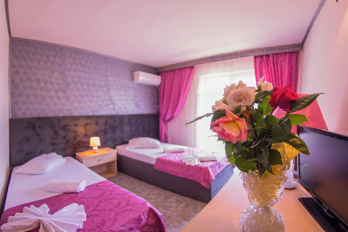 A hotel room with two beds, a TV, a vase with flowers, and a window with curtains.