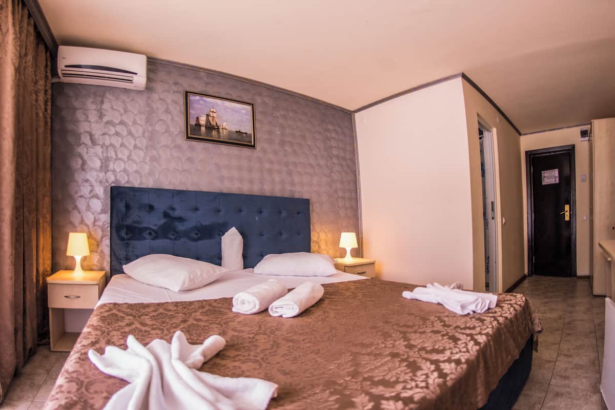 A hotel room with a large bed, two bedside tables with lamps, an air conditioner, and a framed picture on the wall.