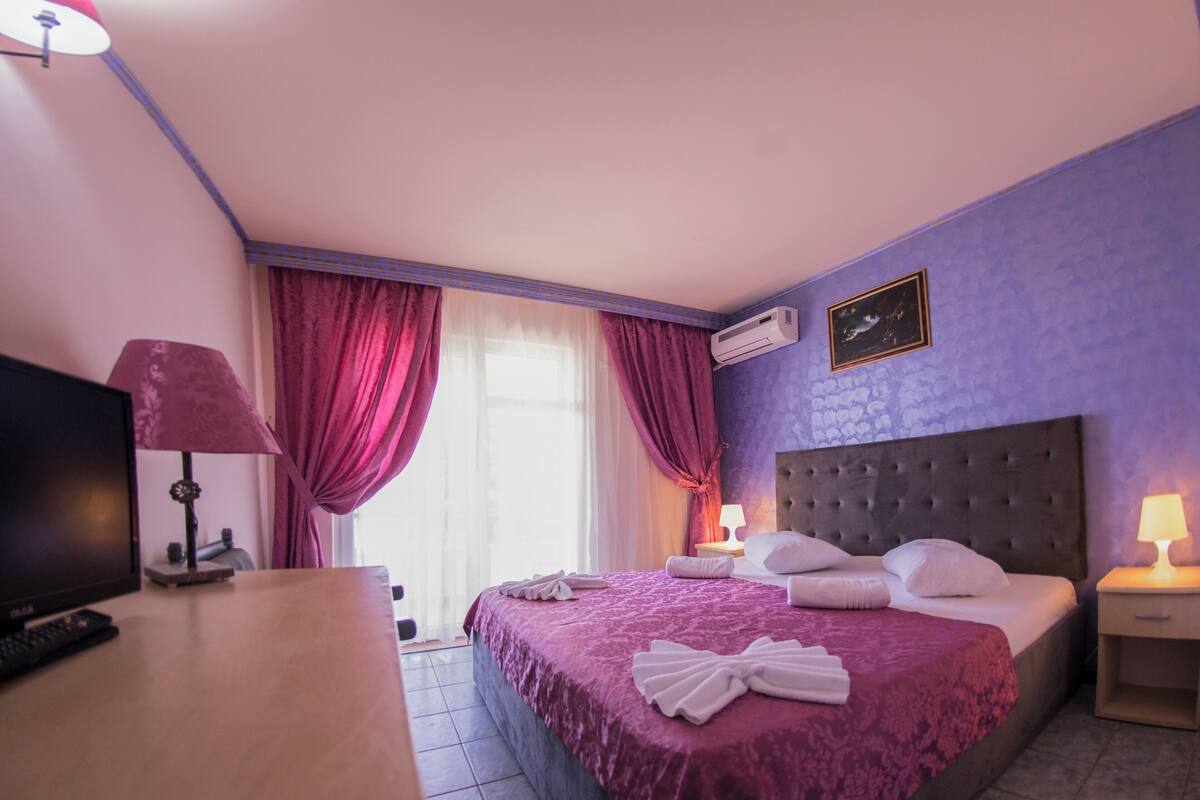 A hotel room with a bed, a TV, a lamp, and an air conditioner.