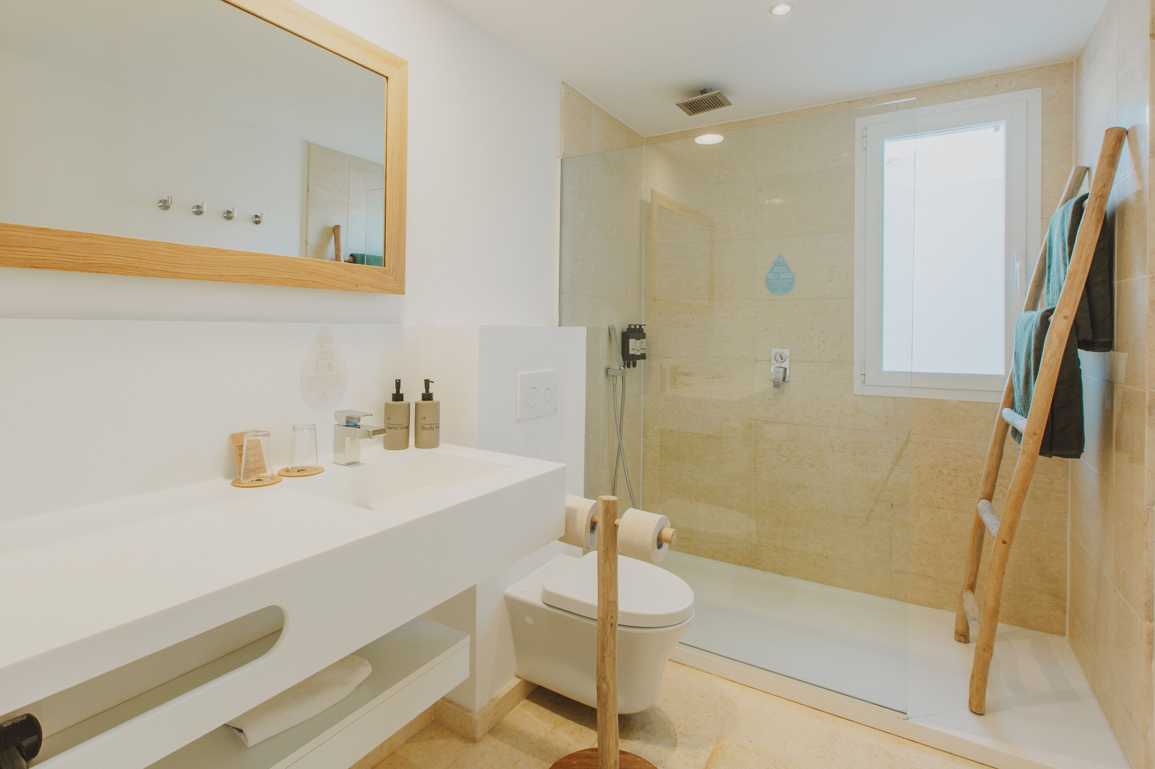 Un bagno moderno con un mobile lavabo bianco, un water, una cabina doccia in vetro e una scala di legno appoggiata al muro.