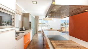 A modern kitchen with a central island, a dining area with a view, and a large window. - Lago Resort Menorca - Villas & Bungalows del Lago (Ciutadella de Menorca)