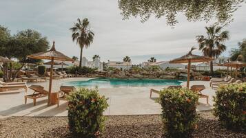 Zona de piscina con sillones de descanso, sombrillas y palmeras.