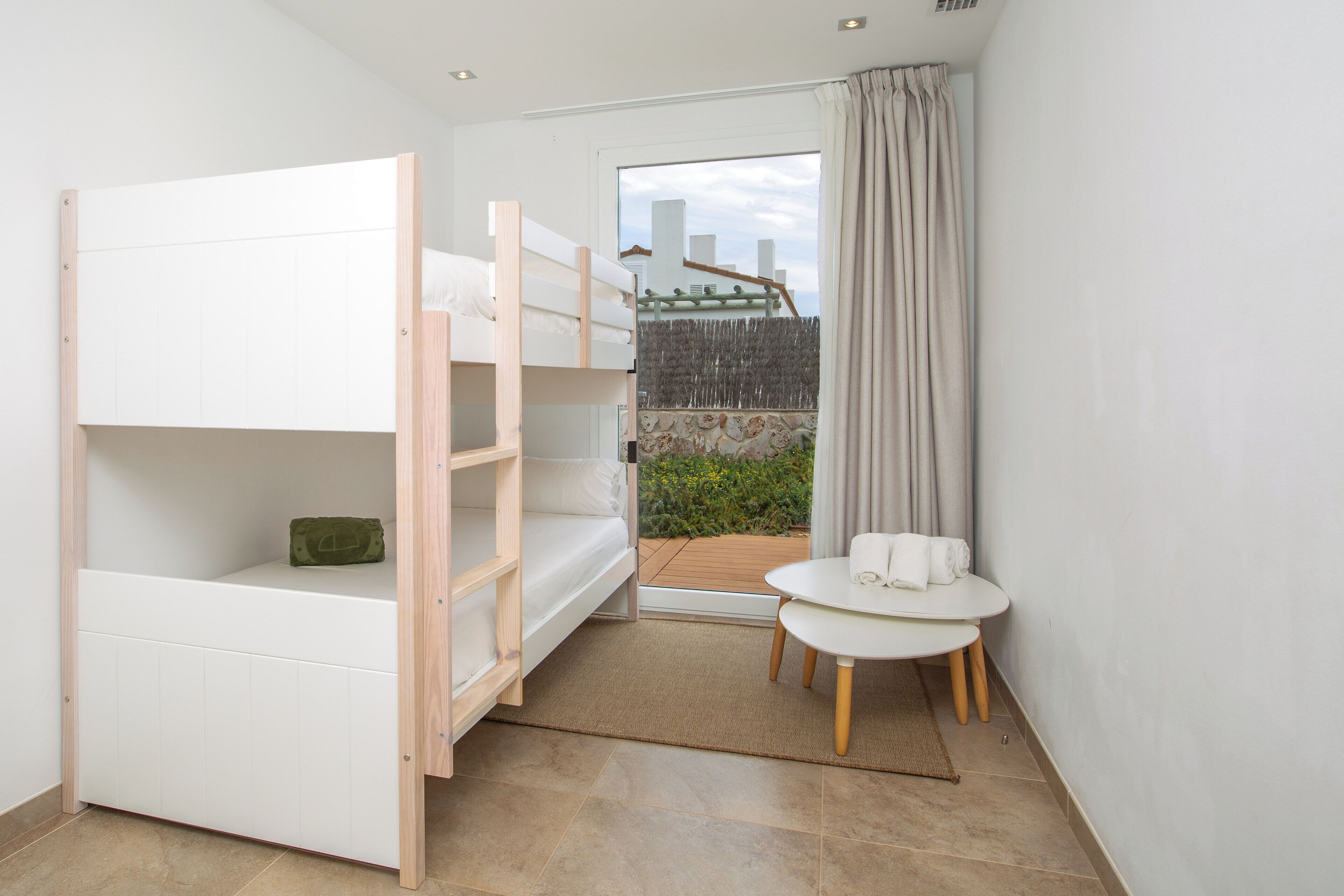 Quarto com beliche, uma mesinha e vista para um jardim através de uma porta de vidro.