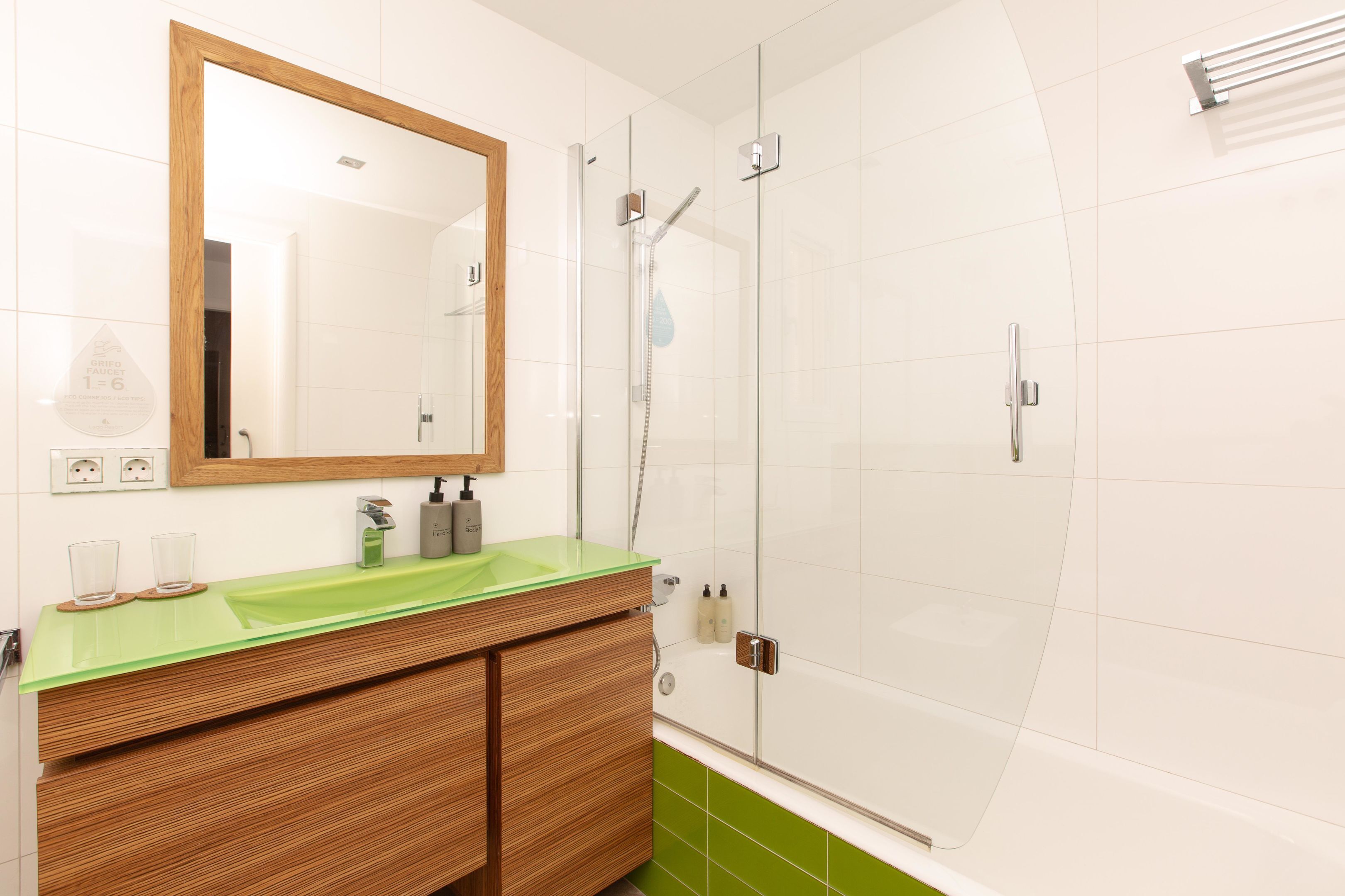 A bathroom with a wooden vanity, a green sink, a mirror, and a glass-enclosed shower.