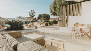 A poolside area with wicker furniture, a table, and a view of the pool and surrounding buildings. - Lago Resort Menorca - Villas & Bungalows del Lago (Ciutadella de Menorca)