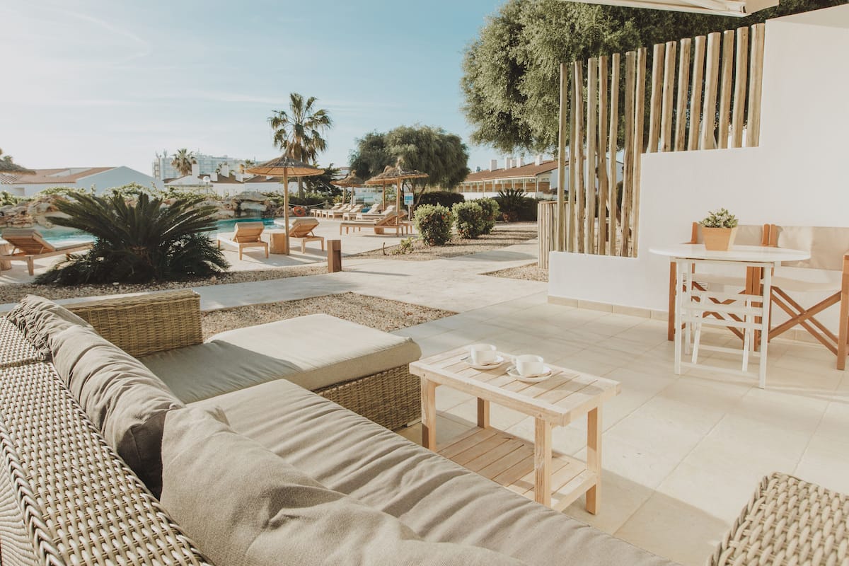 Un espace aménagé au bord de la piscine, avec des meubles en osier, une table et une vue sur la piscine et les bâtiments environnants.