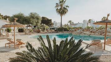 A pool area with lounge chairs and umbrellas, surrounded by palm trees and a rocky landscape.