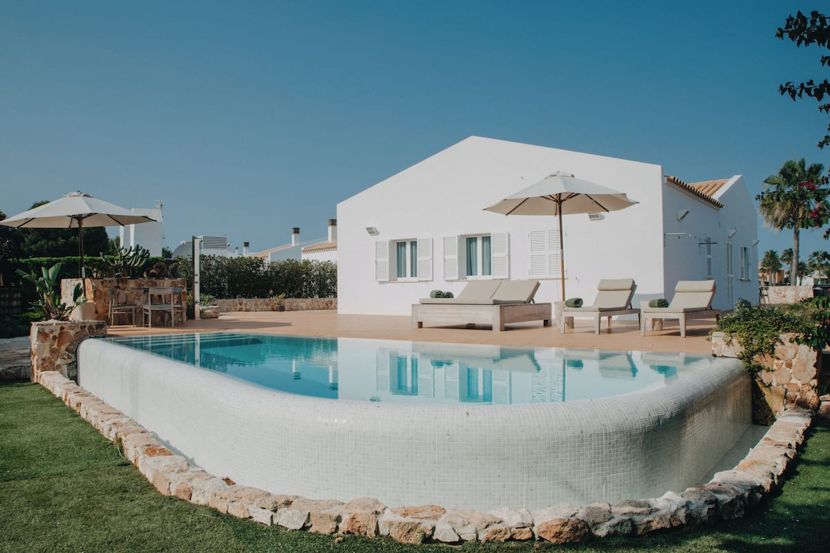 Une villa moderne aux murs blancs, dotée d’une piscine, d’un espace extérieur aménagé et surplombée d’un ciel d’un bleu éclatant.