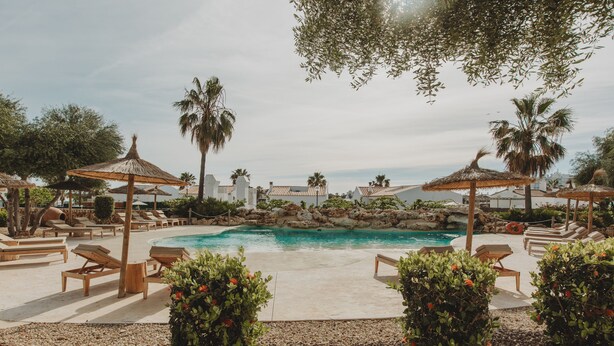 A pool area with lounge chairs and umbrellas, surrounded by greenery and palm trees. - Lago Resort Menorca - Villas & Bungalows del Lago (Ciutadella de Menorca)