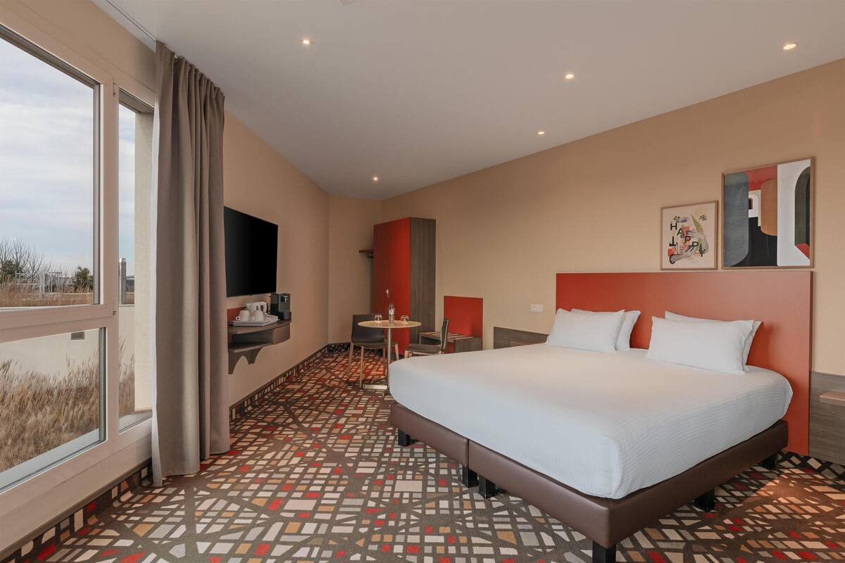 A hotel room with a large bed, a desk, a chair, and a TV.