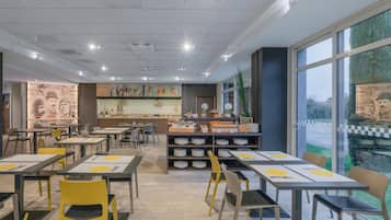 En moderne restaurant med flere borde og stole, en disk med madpræsentationer og store vinduer med udsigt til det fri.