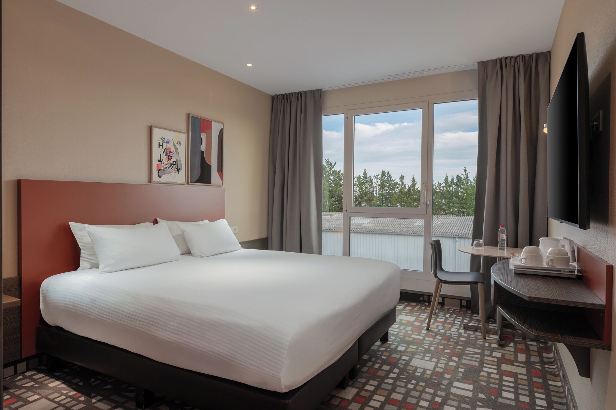 Une chambre d’hôtel avec un grand lit, une petite table avec des tasses et un plateau, une chaise, une télévision et une fenêtre avec des rideaux.