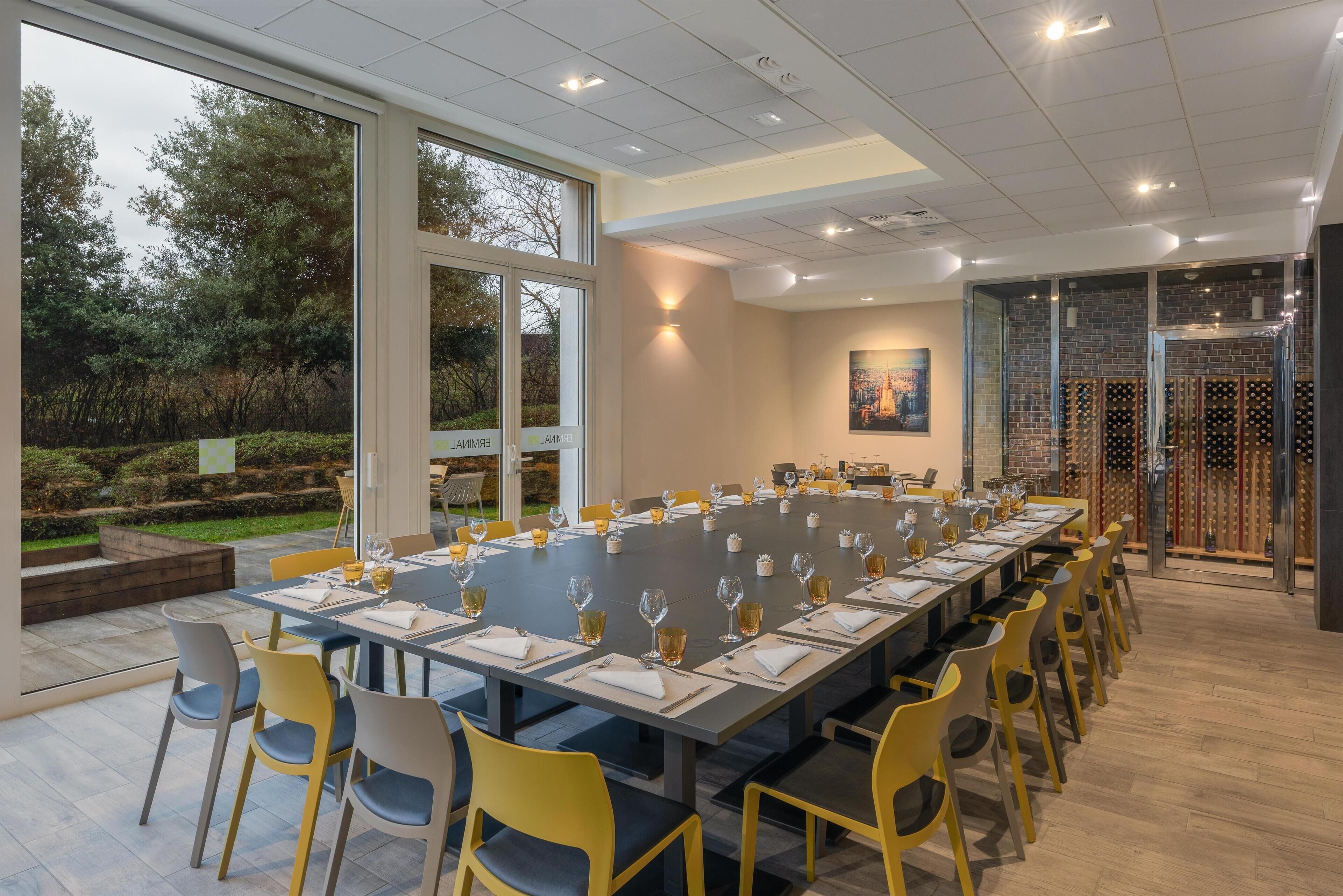 Une salle de conférence avec une longue table préparée pour une réunion, entourée de chaises jaunes.