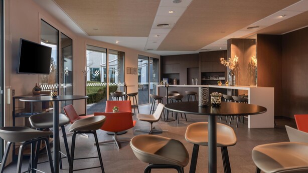 A modern interior with multiple seating areas, including round tables and chairs, and a bar area with a counter.