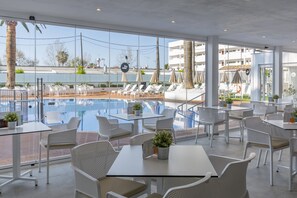 A poolside area with white wicker chairs and tables, a clear view of the pool, and a modern building in the background. - Hotel HSM Linda Playa (Calvia)