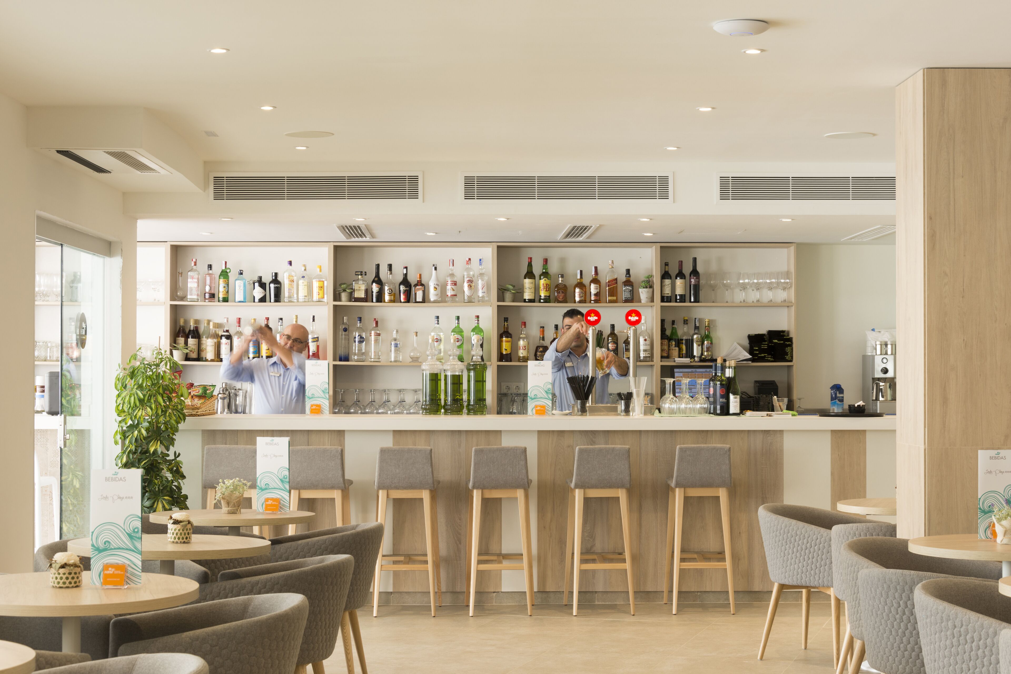 A modern bar area with shelves of various liquor bottles, a bar counter, and several stools.
