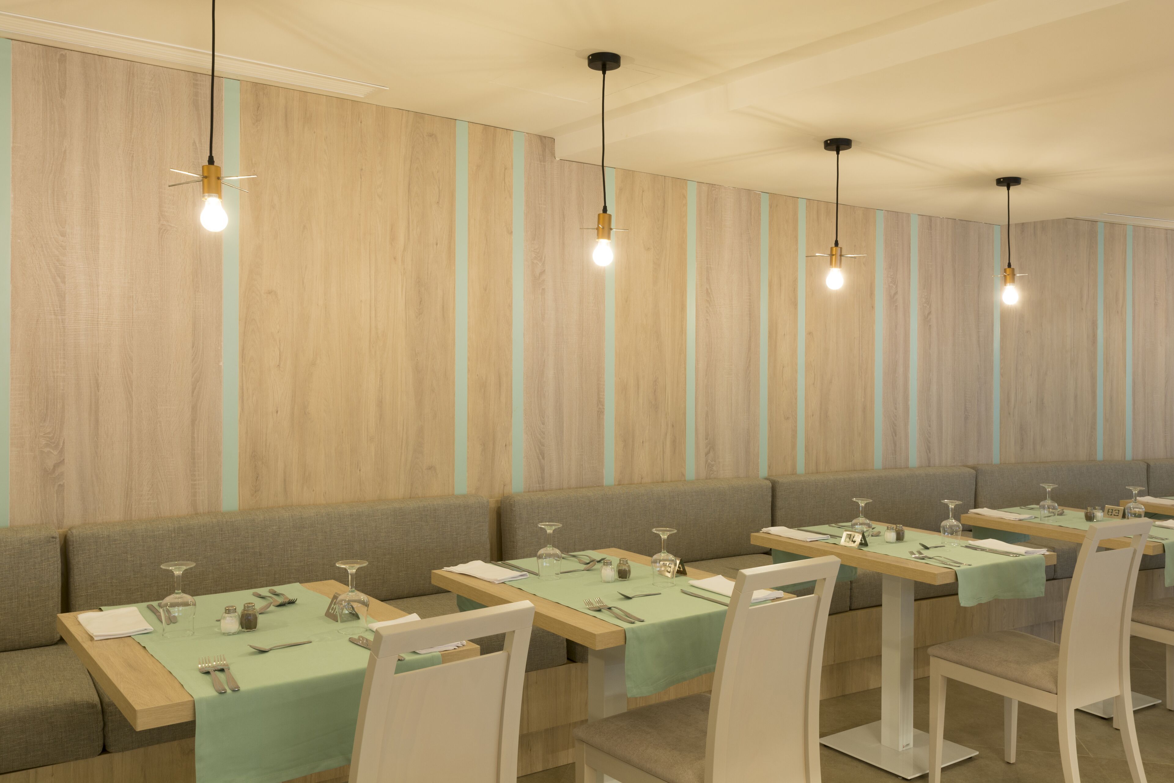 Ein Restaurant mit Holzwandverkleidung, grünen Tischdecken und weißen Stühlen.