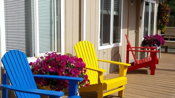 Una terraza de madera con tres sillas Adirondack en azul, amarillo y rojo.
