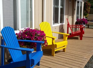 Una terraza de madera con tres sillas Adirondack en azul, amarillo y rojo.