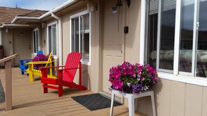 A covered outdoor area with colorful Adirondack chairs, a small table, and a flower arrangement. - Sea Haven Motel & Guest House (Rockaway Beach)