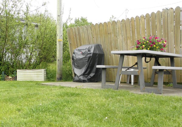 Une table de pique-nique avec des bancs, un barbecue couvert et un arrangement floral dans un jardin.