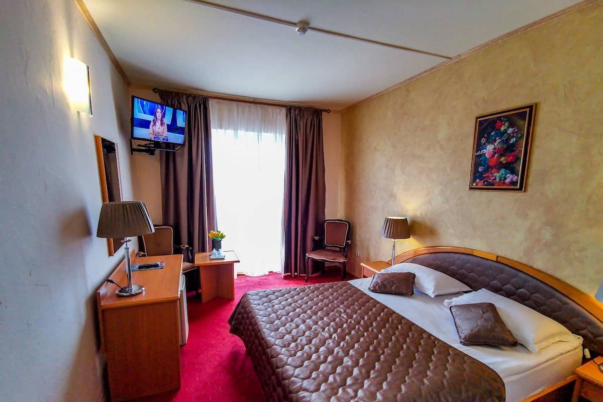 A hotel room with a bed, a desk, a chair, a TV, and a painting on the wall.