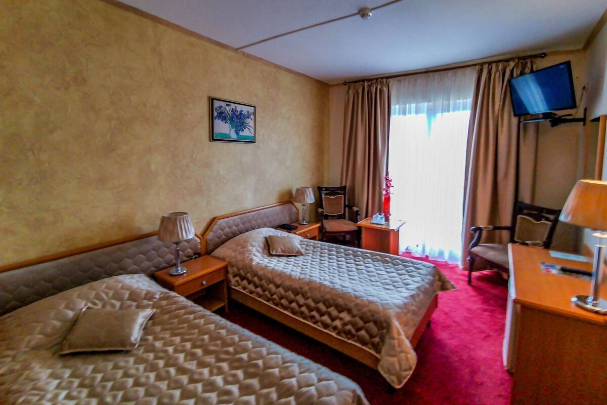 A hotel room with two beds, a desk, a chair, a television, and a window with curtains.