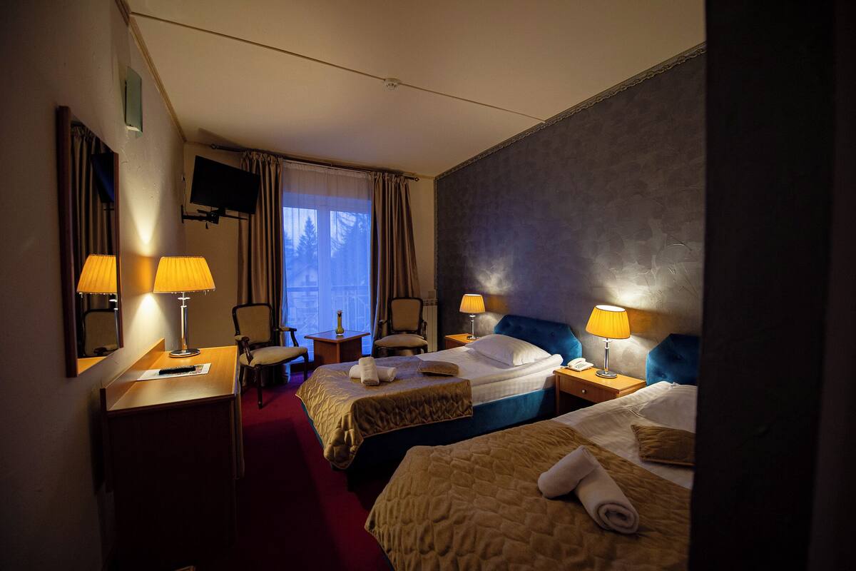 A hotel room with two beds, a desk, a chair, a TV, and a window with curtains.