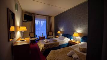 Habitación de hotel con dos camas, un escritorio, una silla, un televisor y una ventana con cortinas.