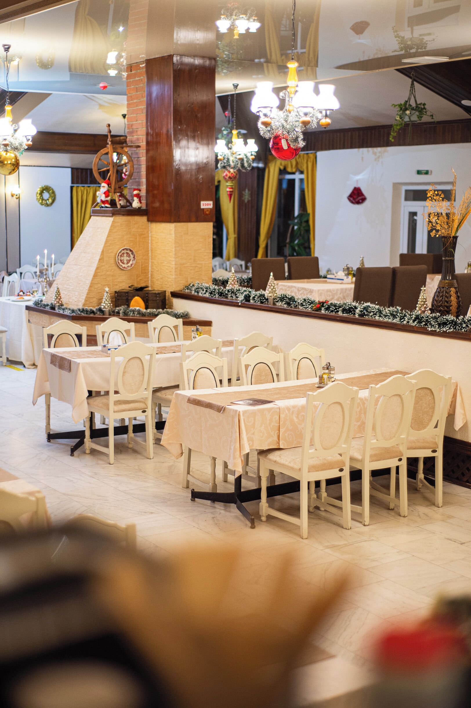 A restaurant with multiple tables and chairs, a brick column, and a Christmas tree decoration.