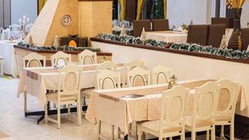 A restaurant with multiple tables and chairs, a brick column, and a Christmas tree decoration.