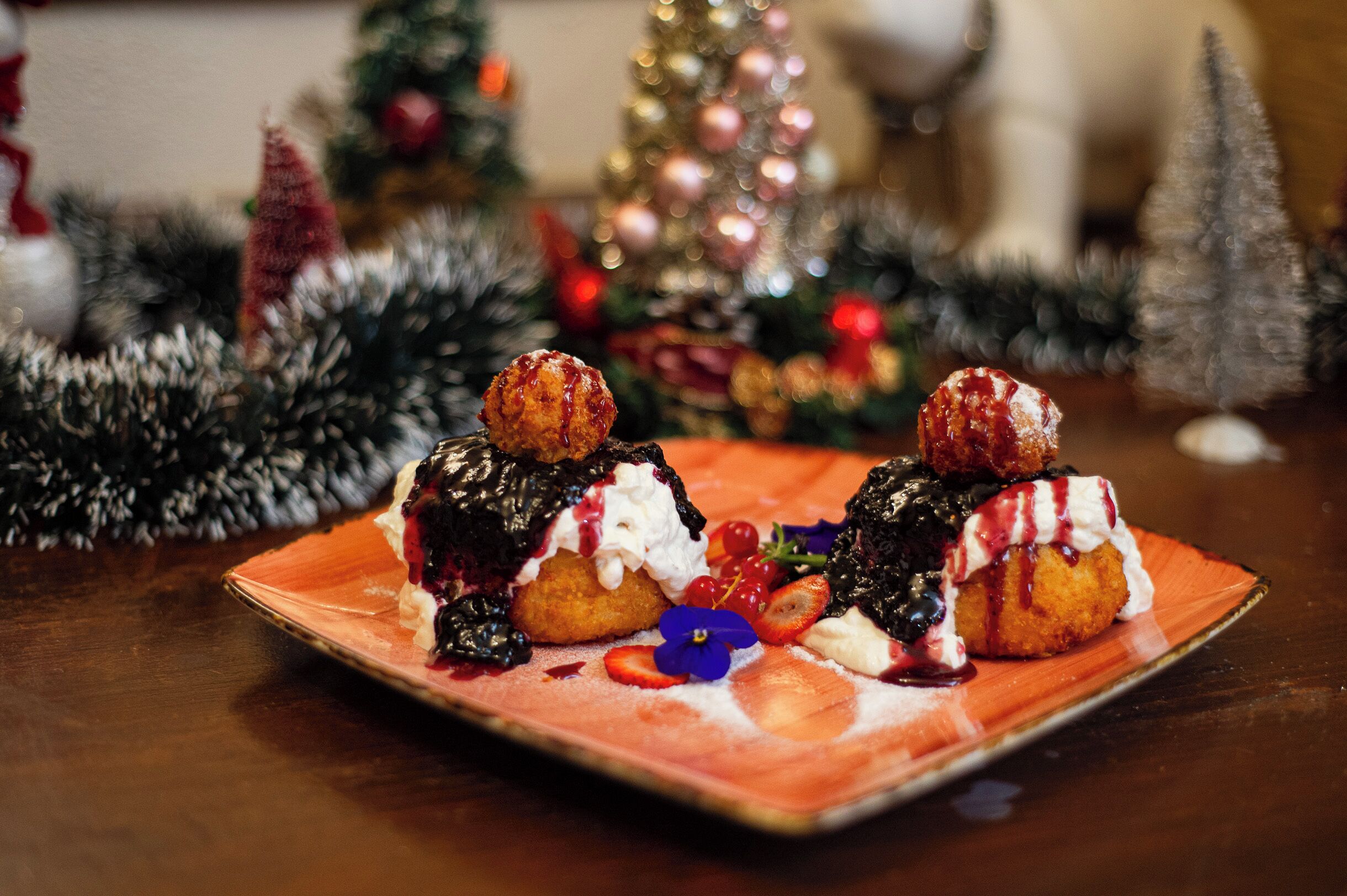 A dessert plate with two pastries topped with whipped cream and berries, set against a festive background with a Christmas tree and decorations.
