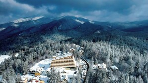Estância de esqui coberta de neve, com um edifício imponente e varandas múltiplas, e uma pista de esqui em primeiro plano.