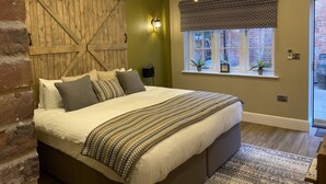 A bedroom with a large bed, a wooden barn door wall, a hanging light fixture, and a window with a view of the outside. - The Boot at Repton (Derby)