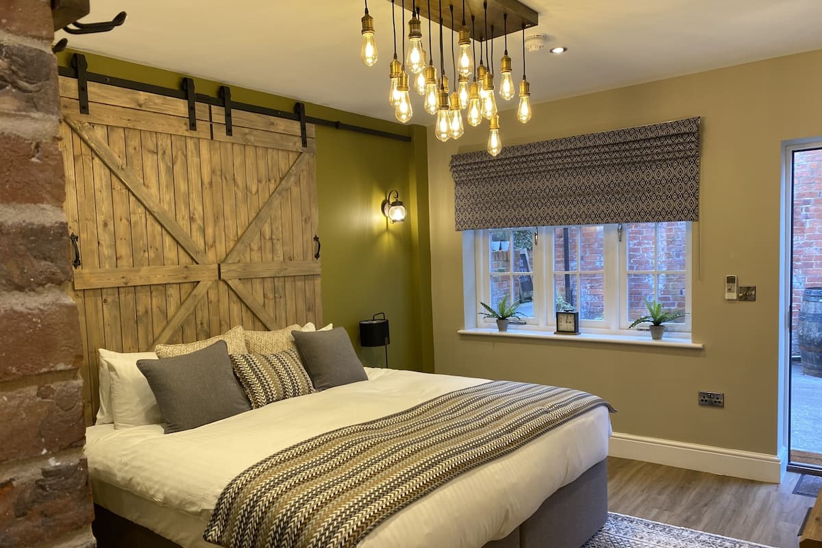 Un dormitorio con una cama grande, una pared decorada con una puerta de madera rústica, una lámpara colgante y una ventana con vistas al exterior.