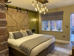A bedroom with a large bed, a wooden barn door wall, a hanging light fixture, and a window with a view of the outside. - The Boot at Repton (Derby)