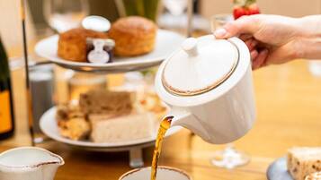 A tea service with a teapot pouring into a cup, a tiered dessert stand, and a table with plates of scones and pastries.